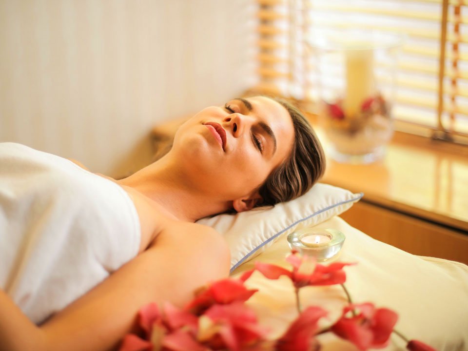 Woman laying on a bed wrapped in a towel at a spa